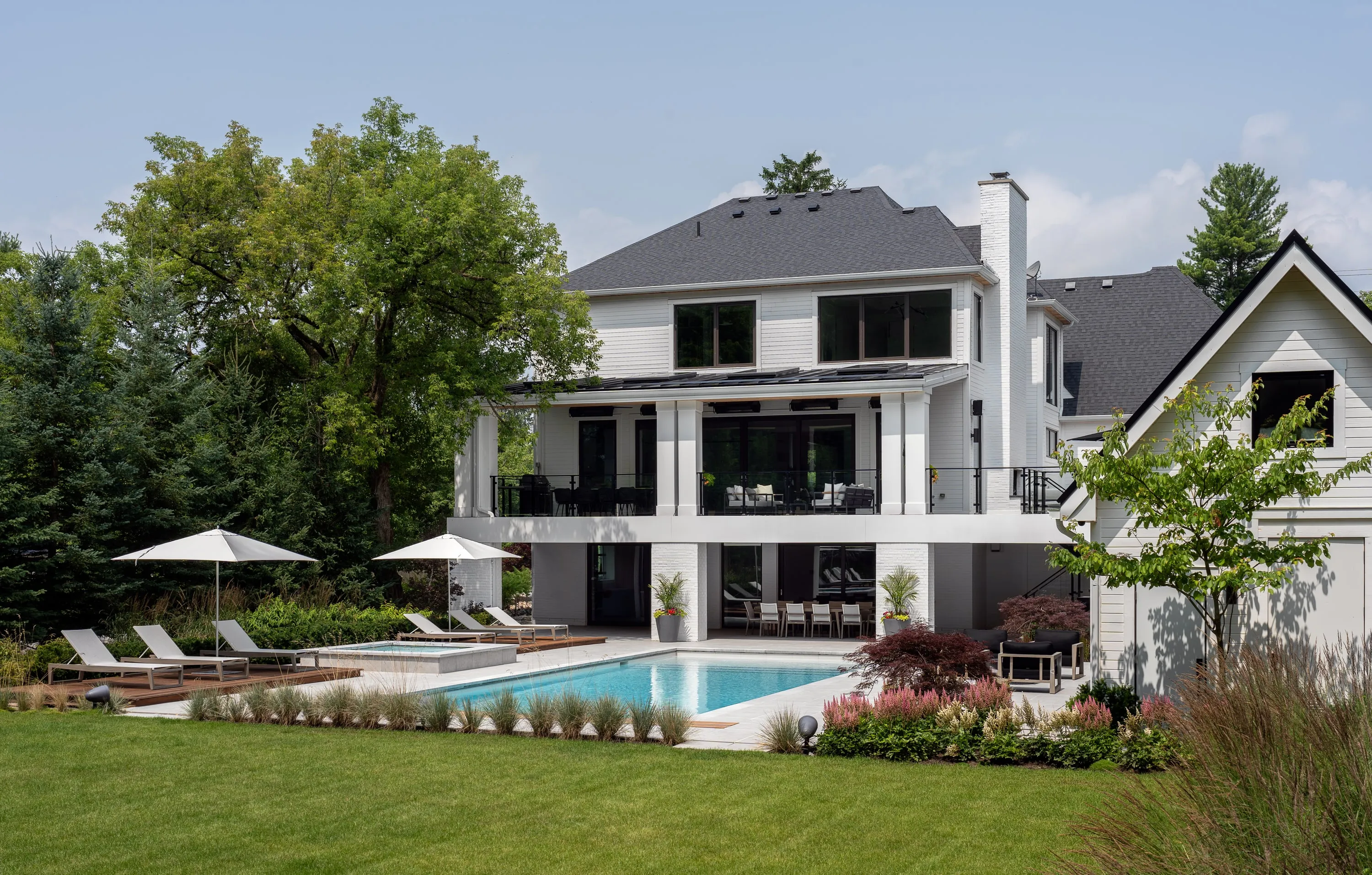 White gabled residence with a pool and pool house, seen across the lawn.