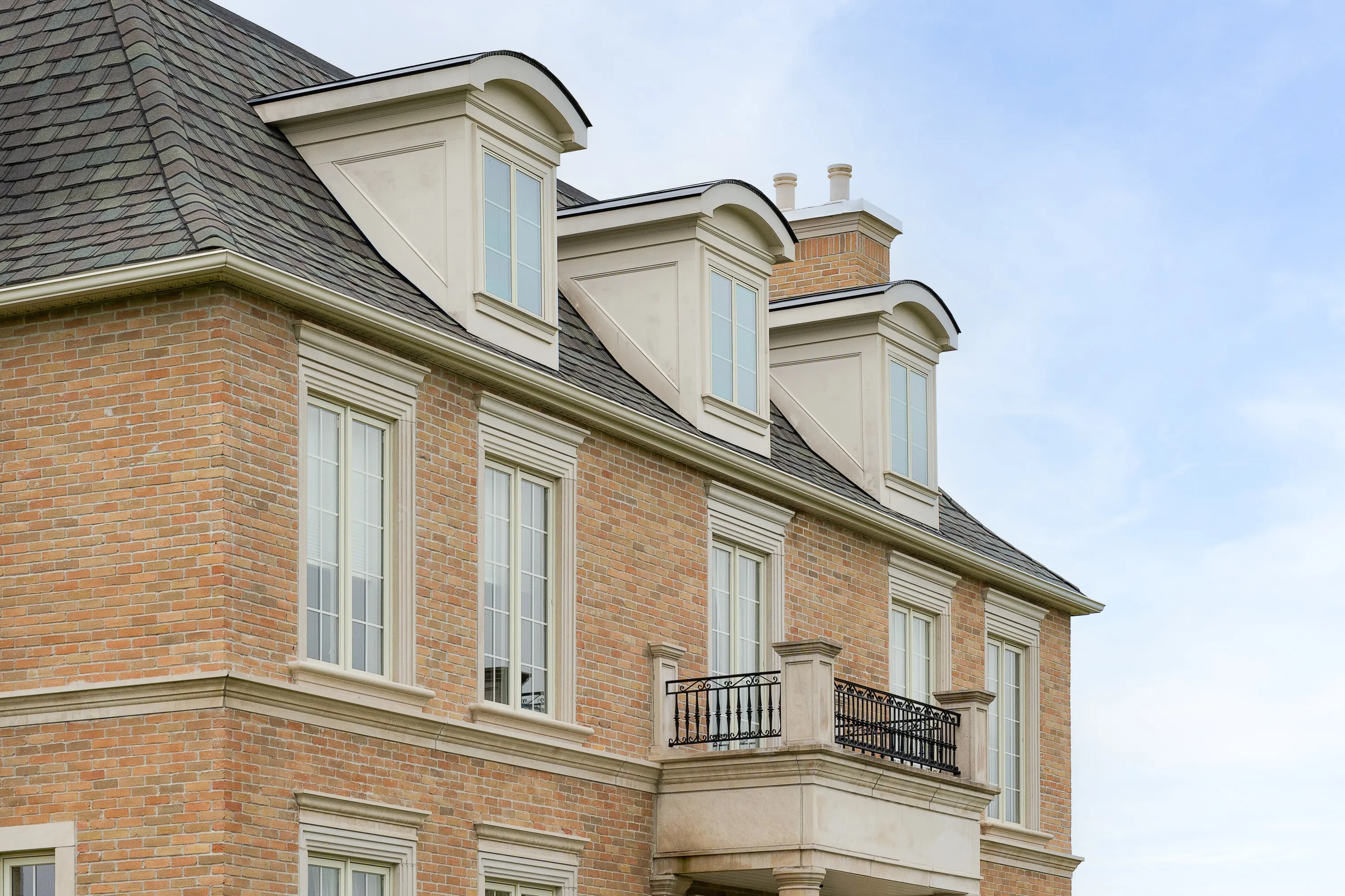 Barrel dormers and a stone balcony over the garage wing.