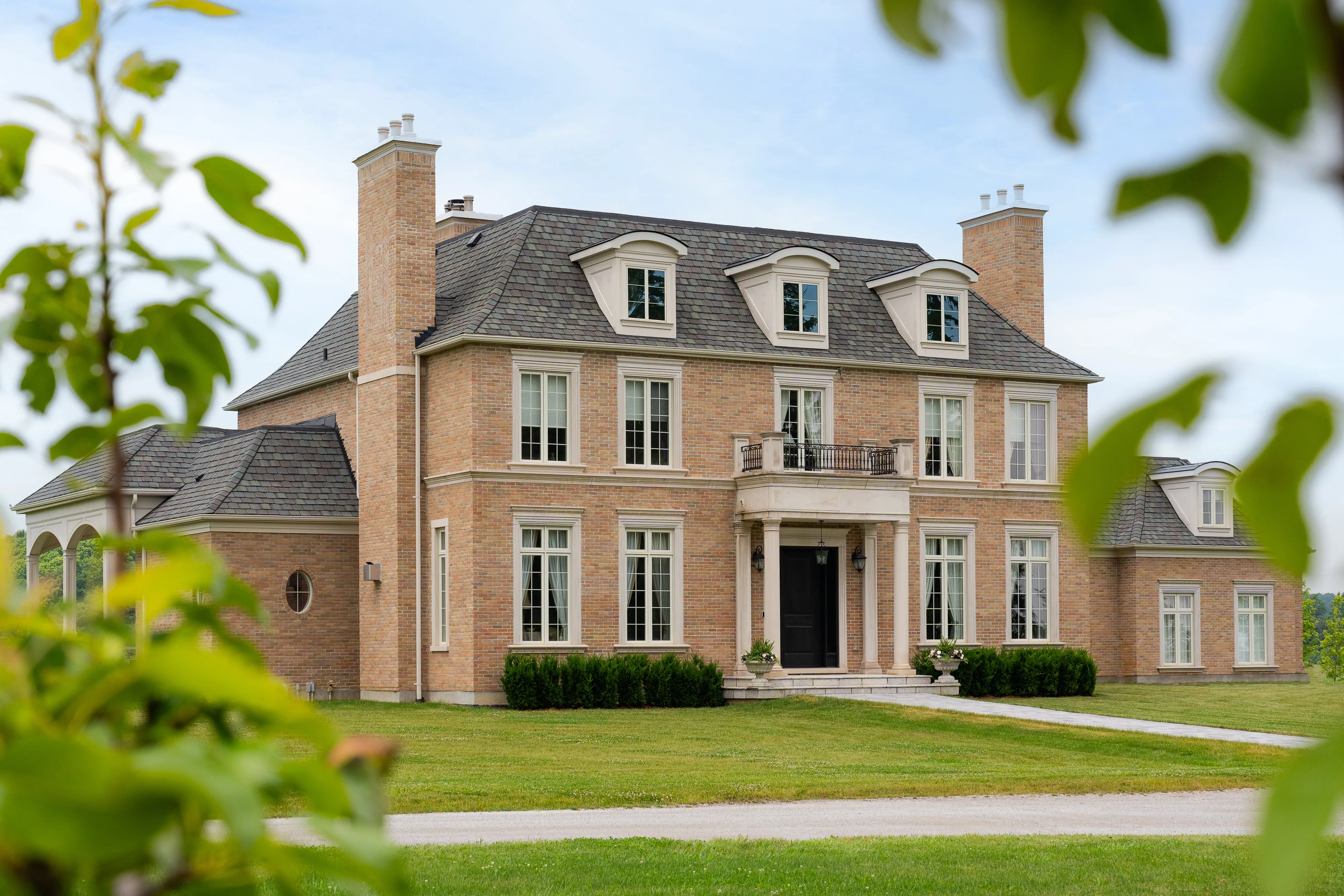 Brick residence with a slate-toned roof, dormers and an arched breezeway, set in open lawn.